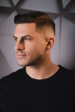 Handsome man with trendy hairstyle near dark wallの写真素材