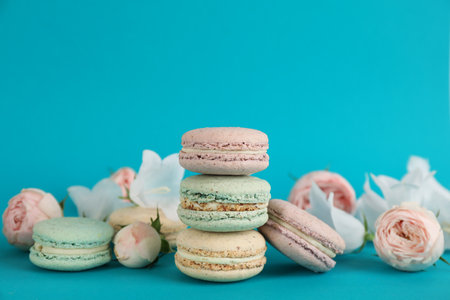 Delicious macarons and flowers on light blue background, space for textの写真素材