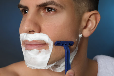 Handsome man shaving with razor on blue background, closeupの写真素材
