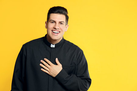 Priest in cassock with clerical collar laughing on yellow background. Space for textの写真素材