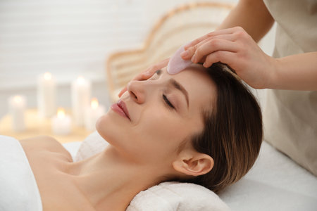 Young woman receiving facial massage with gua sha tool in beauty salonの写真素材