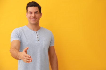 Man offering handshake against yellow background, focus on hand. Space for textの写真素材