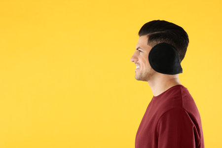 Man wearing stylish earmuffs on yellow background. Space for textの写真素材