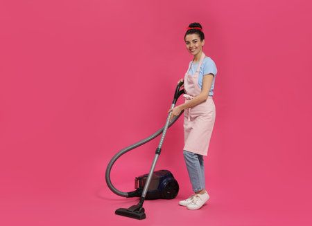 Housewife with vacuum cleaner on pink backgroundの写真素材