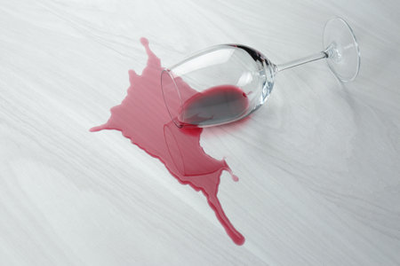 Overturned glass and spilled wine on white wooden tableの写真素材