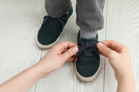 Mother helping son to tie shoe laces at home, closeupの写真素材