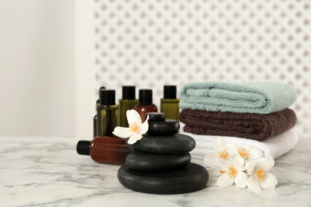 Black spa stones, beautiful jasmine flowers, towels and skin care products on white marble tableの写真素材