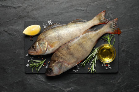 Fresh raw perches and ingredients on black slate table, top view. river fish