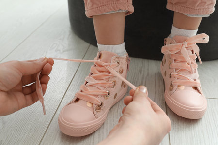 Mother helping daughter to tie shoe laces at home, closeupの写真素材