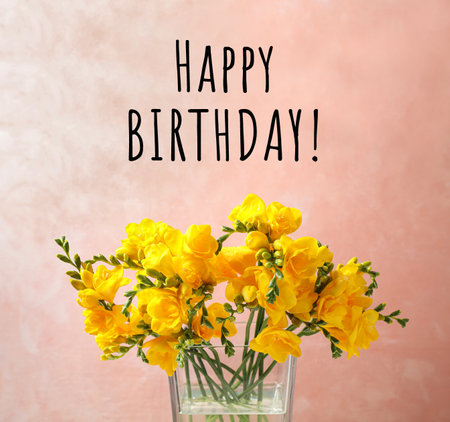 Happy Birthday! Beautiful yellow freesia flowers in glass vase against pink backgroundの写真素材