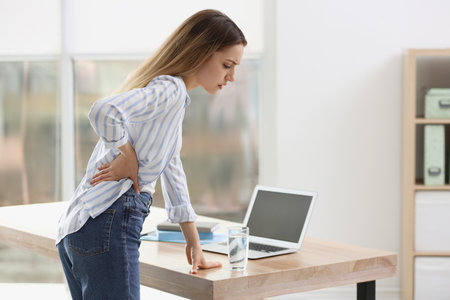 Woman suffering from back pain in office. Symptom of bad postureの写真素材