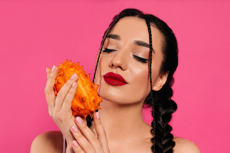 Young woman with fresh kiwano on pink background. exotic fruitsの写真素材