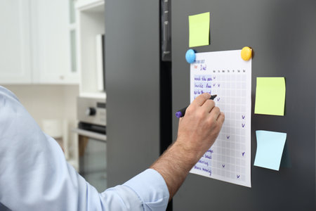 Man checking to do list on fridge in kitchen, closeupの写真素材
