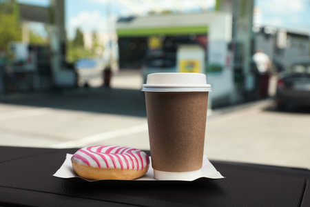 Paper coffee cup and doughnut on car dashboard at gas stationの写真素材