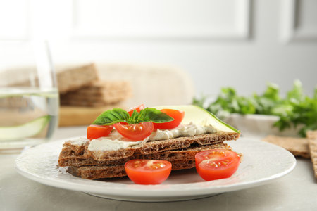 Fresh rye crispbreads with cream cheese and vegetables on light grey table, closeupの写真素材