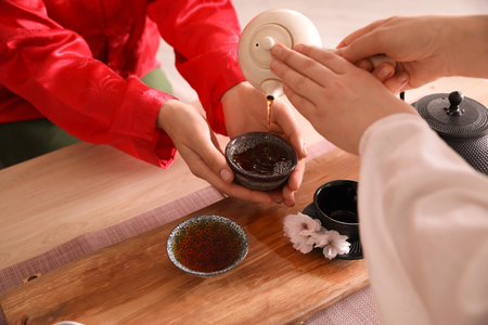 Master pouring freshly brewed beverage into guest's cup during traditional tea ceremony at table, closeupの写真素材