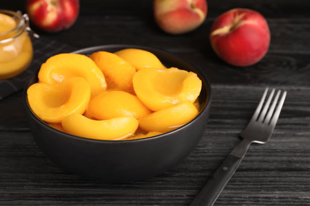Canned peach halves and fork on black wooden tableの写真素材