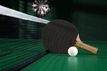 Black racket and ball on green table tennis table indoorsの写真素材