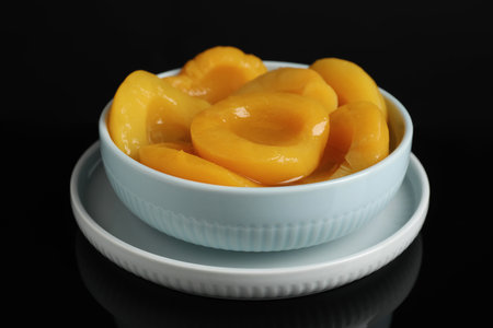 Canned peach halves in bowl on black backgroundの写真素材
