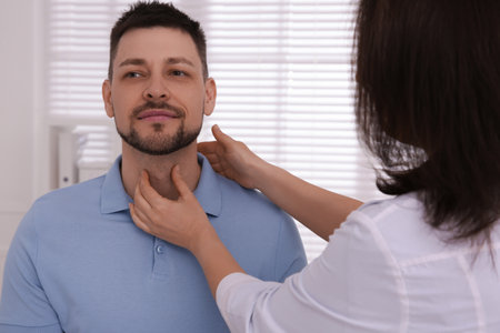 Doctor examining thyroid gland of patient indoors