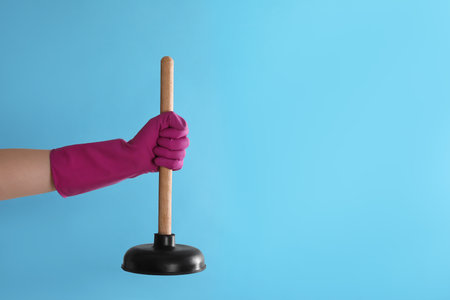 Woman holding plunger on turquoise background, closeup. Space for textの写真素材