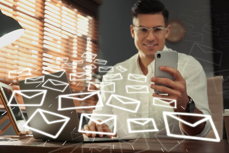 Businessman sending emails at table indoors, focus on handの写真素材