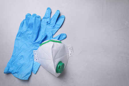 Protective medical gloves and respirator on light grey stone background, flat lay with space for textの写真素材