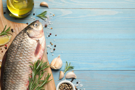 Fresh raw crucian carp and ingredients on light blue wooden table, flat lay with space for text....