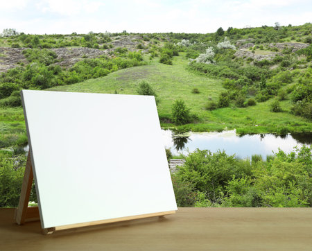 Wooden easel with blank canvas on table and beautiful view of rocky hill. Space for textの写真素材