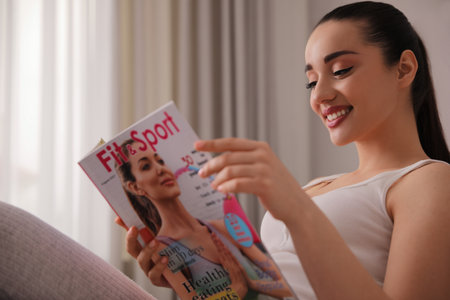 Happy young woman reading modern magazine indoorsの写真素材