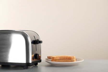 Electric toaster with bread slices on light table. Space for text
