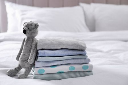 Stack of clean baby's clothes and toy on bedの写真素材