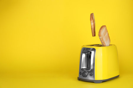 Bread slices popping up out of electric toaster on yellow background. Space for textの写真素材
