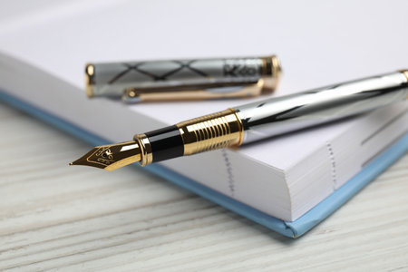 Beautiful fountain pen with ornate nib and notebook on white wooden table, closeupの写真素材