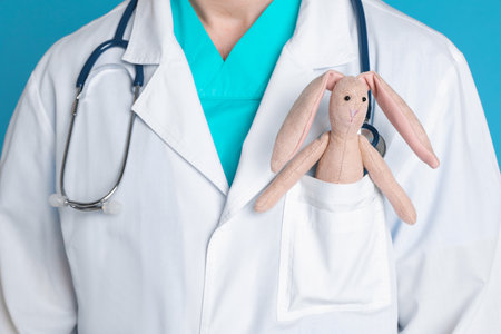 Pediatrician with toy bunny and stethoscope on light blue background, closeupの写真素材
