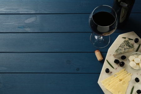 Tasty red wine and different sorts of cheese on blue wooden table, flat lay. Space for textの写真素材