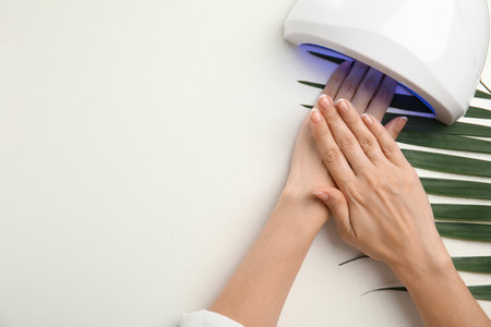 Woman using ultraviolet lamp to dry gel nail polish on white background, top view. Space for textの写真素材