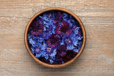 Beautiful colorful cornflowers in bowl on wooden table, top viewの写真素材