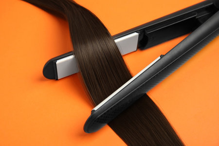 Straightener with brown hair lock on orange background, closeupの写真素材