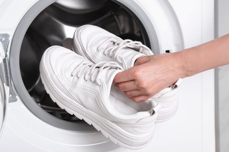 Woman putting pair of sport shoes into washing machine, closeupの写真素材