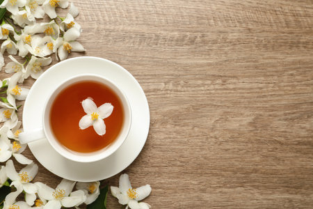 Cup of aromatic jasmine tea and fresh flowers on wooden table, flat lay. Space for textの写真素材