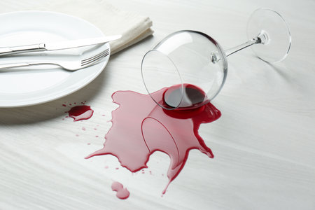 Overturned glass and spilled wine on white wooden tableの写真素材