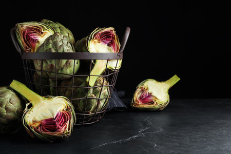 Cut and whole fresh raw artichokes on black table, space for textの写真素材