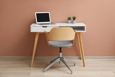 Stylish workplace with laptop and comfortable chair near beige wall indoors. interior designの写真素材