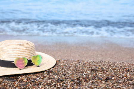 Straw hat and colorful heart shaped sunglasses on sea beach. Space for textの写真素材