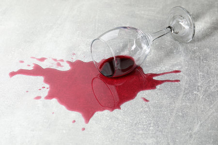 Overturned glass with red wine spill on gray tableの写真素材