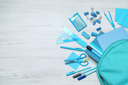 Flat lay composition with backpack and school stationery on white wooden background, space for text