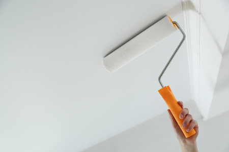Woman painting ceiling with white dye indoors, closeup. Space for textの写真素材