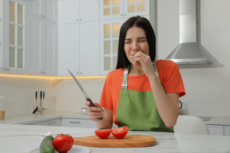 Young woman cutting finger with knife while cooking in kitchenの写真素材
