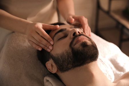 Young man receiving facial massage in beauty salonの写真素材